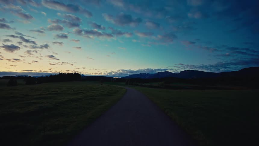 Narrow road crossing a field at dusk with mountains in the background