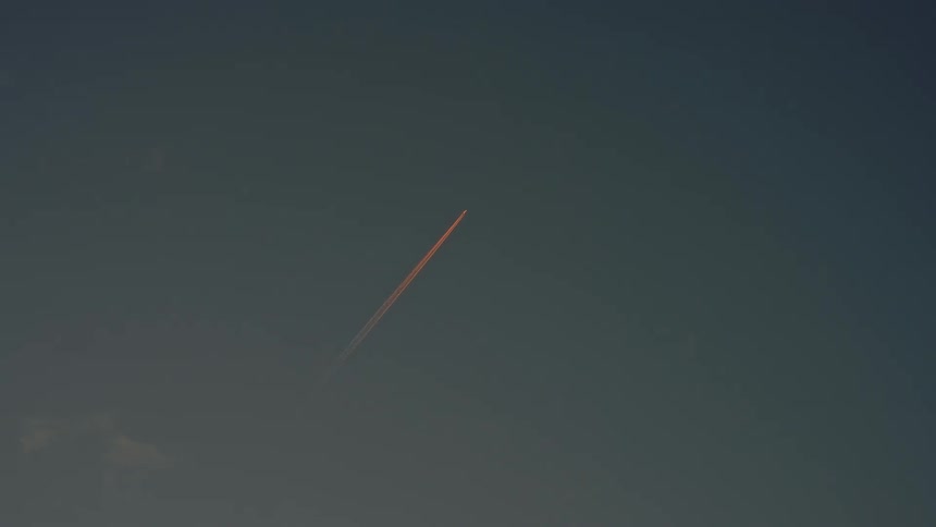 Reddish jet trail streaking across the sky at sunset