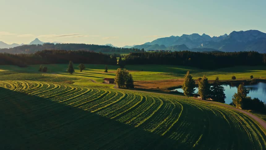 Highway winding through the countryside near a forest and mountains passes a lake and a rural house