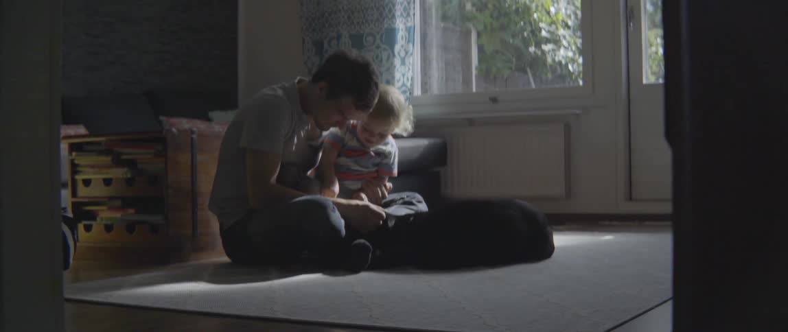 A man, a toddler, and a dog are sitting on a floor in a home