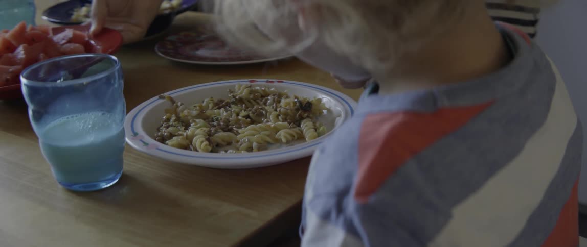 A young toddler boy eats a plate of fresh pasta with a silver fork.