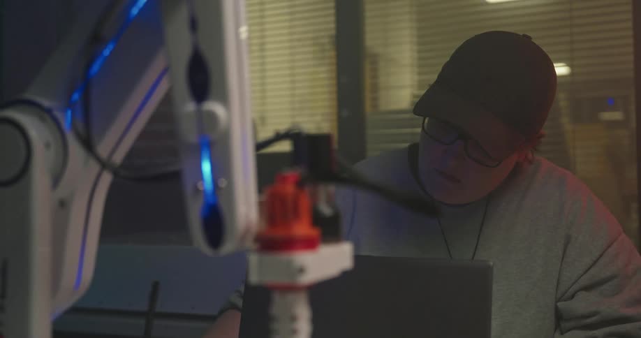 Person using a laptop next to an illuminated robotic arm in a laboratory setting