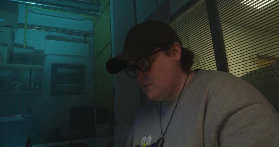 Person operates a laptop beside a white robotic arm with blue lights in a laboratory