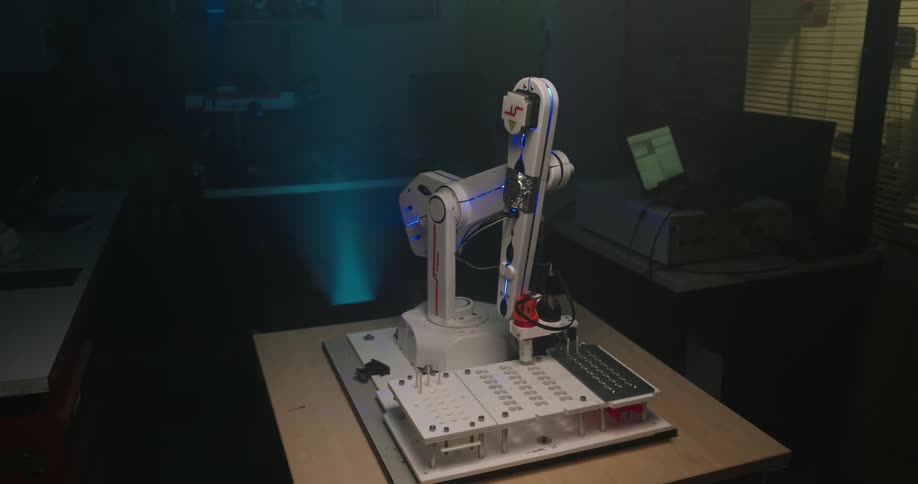 A white and blue robotic arm is prominently featured in a midshot performing intricate movements on a control board on a desk the environment is darkly lit with subtle blue and cyan light illuminating the robots work area