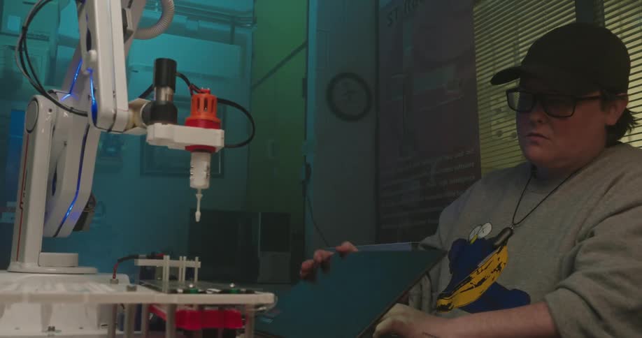 Person working on a laptop next to a robotic arm in a laboratory