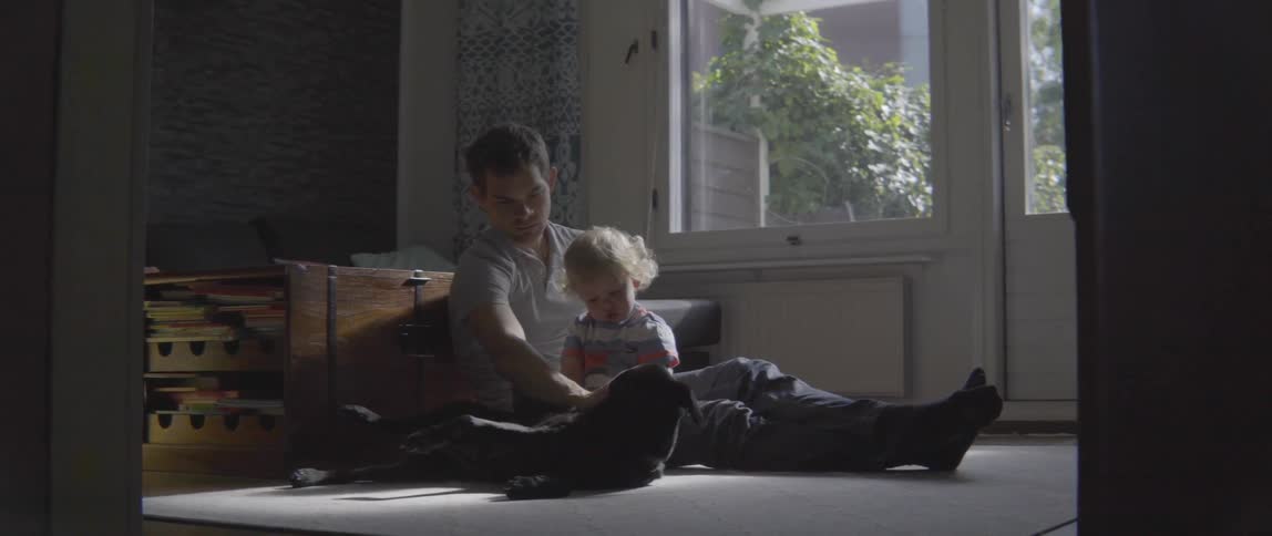 Young father and toddler boy pet their dog while sitting together on a rug.