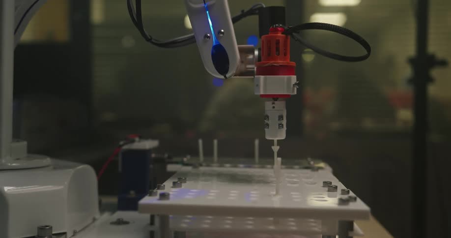A small precise robotic arm performing an automated task over a modular test bed in a dimly lit high tech lab