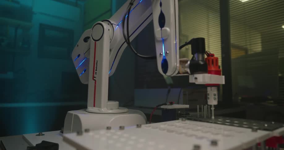 Robotic arm with precision tool positioned over perforated surface in industrial setting with window reflections