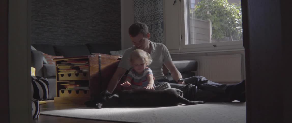 Young father supervising his toddler son as they play with a domestic dog indoors.