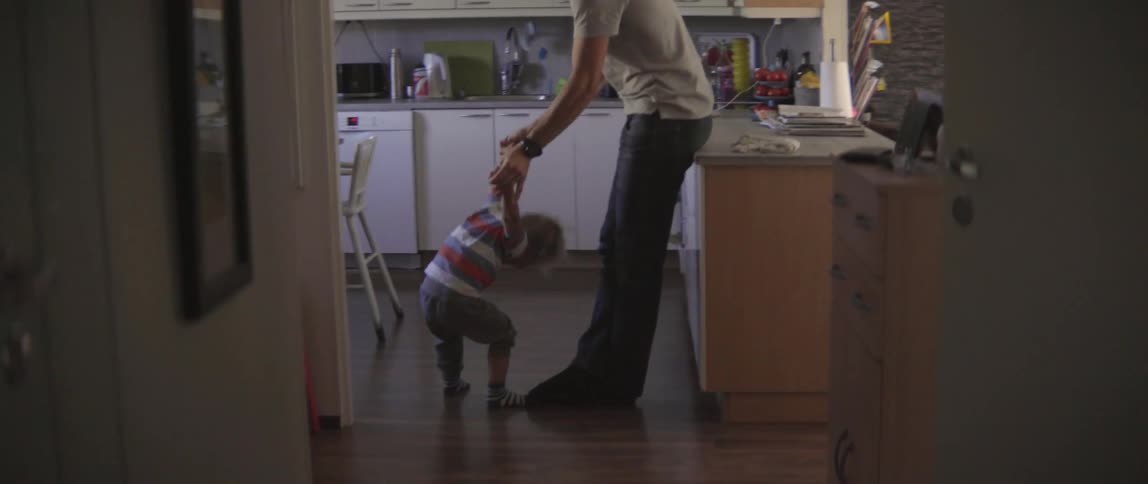 A toddler rolls back and does a somersault against the legs of the man holding his arms