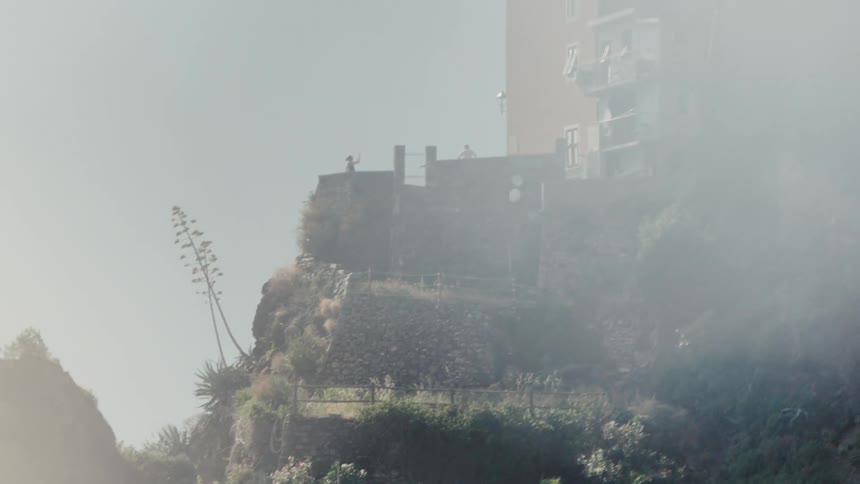 Houses built on a cliff appear partially covered by mist