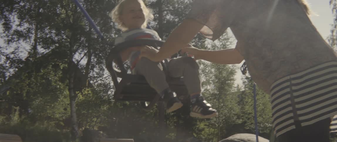 Happy toddler boy swinging back and forth during a sunny afternoon at the park.
