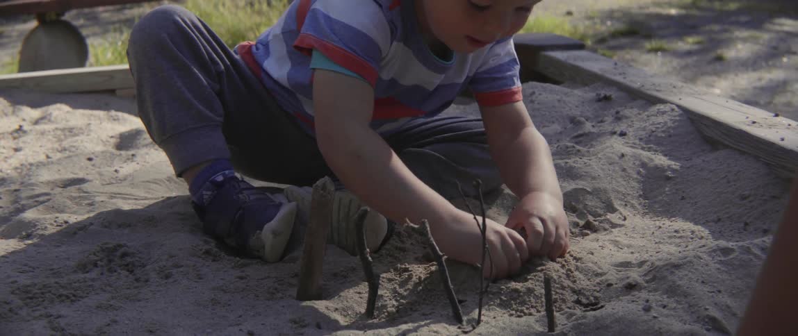 Young toddler boy focused on sensory play while sitting in a sunny sand pit.