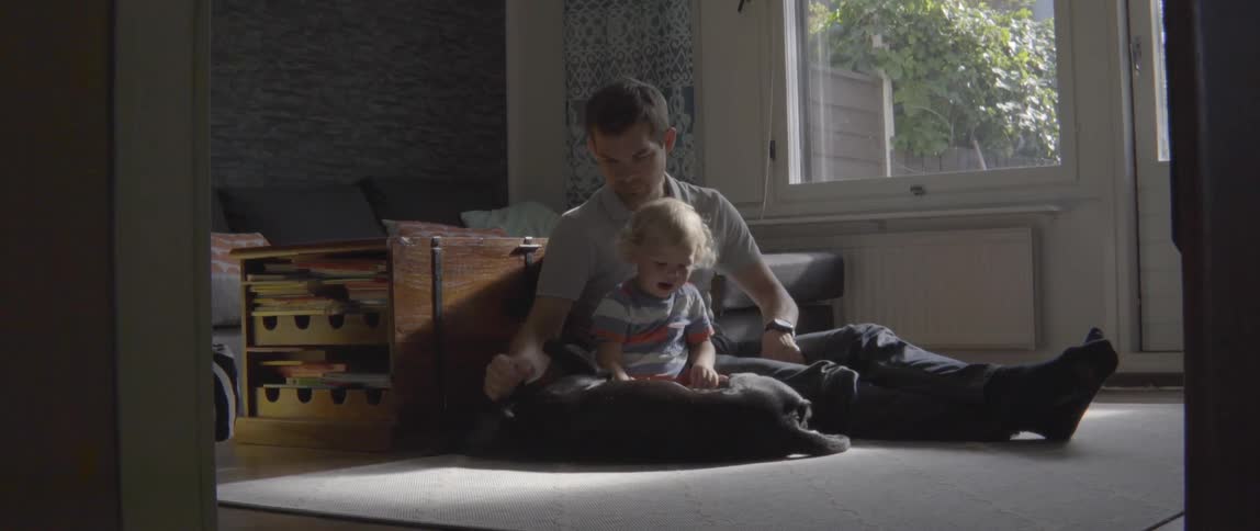 Young father and toddler boy pet their dog while sitting together on a rug.