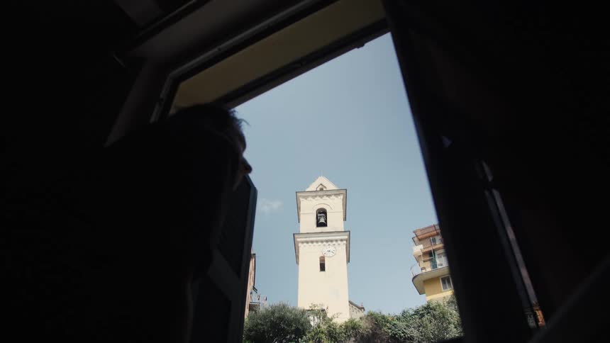 A young man looking outdoors through a window in a building in a suburban city during daytime