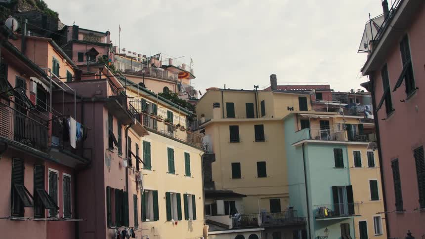 A highangle shot captures the colorful facades of multistory italianstyle apartment buildings with terra cotta roofs balconies and dark wooden shutters the densely packed buildings climb up a hillside under a hazy overcast sky