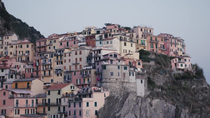 The colorful houses of a picturesque village cling dramatically to a steep cliff face overlooking the sea at dusk