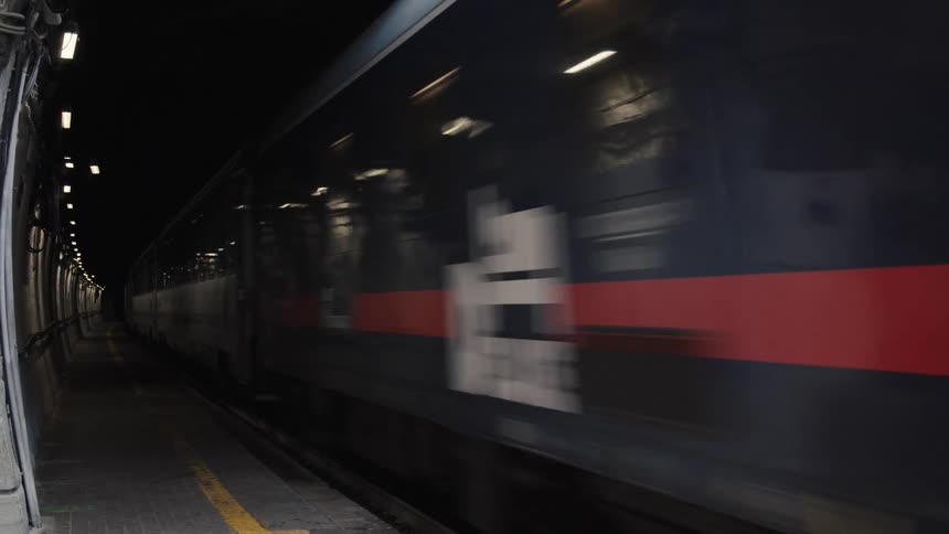 Highspeed train exits a tunnel and passes through a station platform
