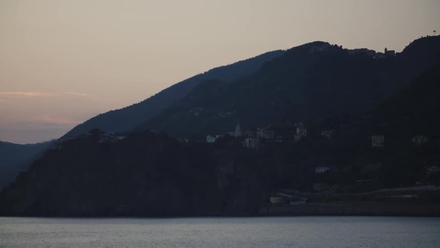 Dark hills at dusk with scattered buildings near the calm sea