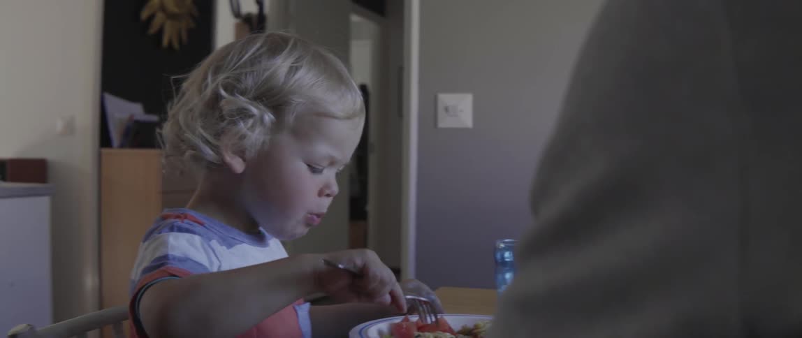 Young toddler boy sitting at a table while eating pasta for a family meal.