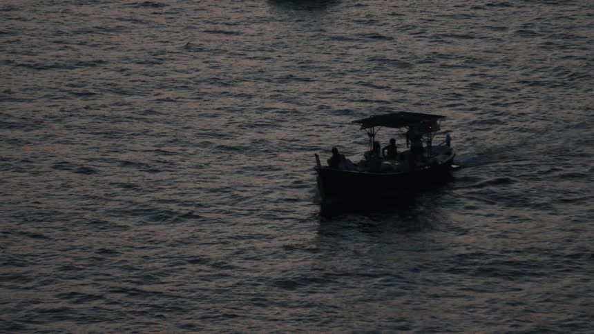 Two boats floating on the sea at sunset one of them with people on board