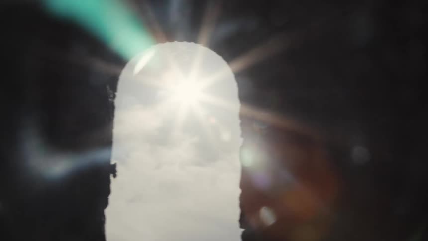 A strong sun lighting shines through a narrow vertical opening in a dark structure creating a bright white silhouette and intense lens flare effects across the blackened frame