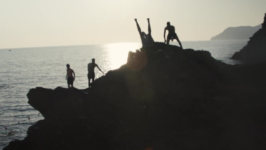 People on a rocky cliff by the sea at sunset