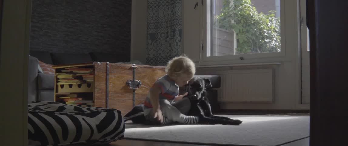 Happy toddler boy embracing a loyal black dog while playing on the ground at home.