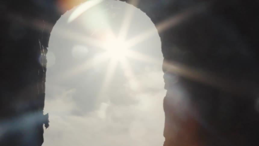 A dark video shows a bright sunburst shining through an archshaped opening causing a strong lens flare and gradually obscuring the silhouette of the opening before the view returns to dark abstract lens flares