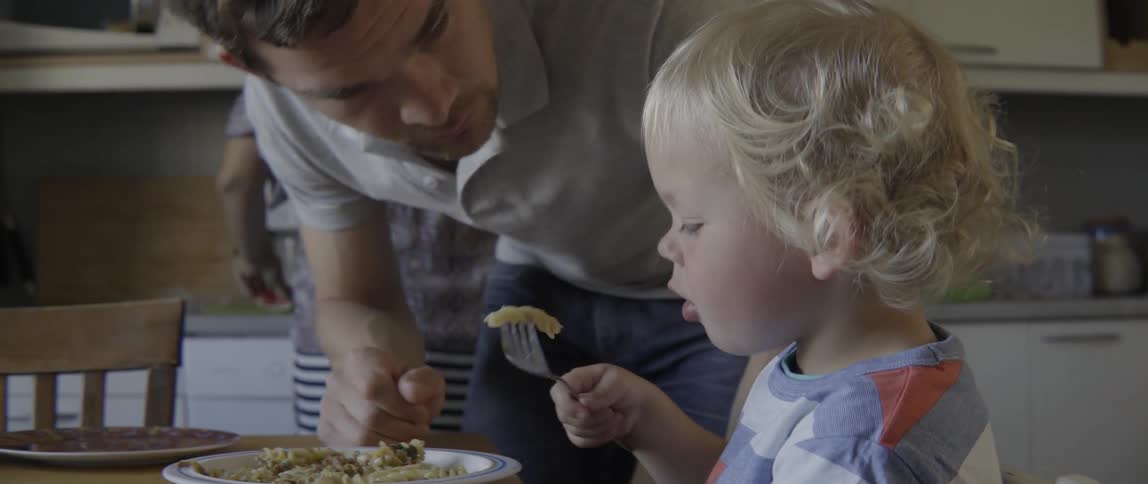 Happy toddler boy tasting a meal while his parent watches in a bright room.