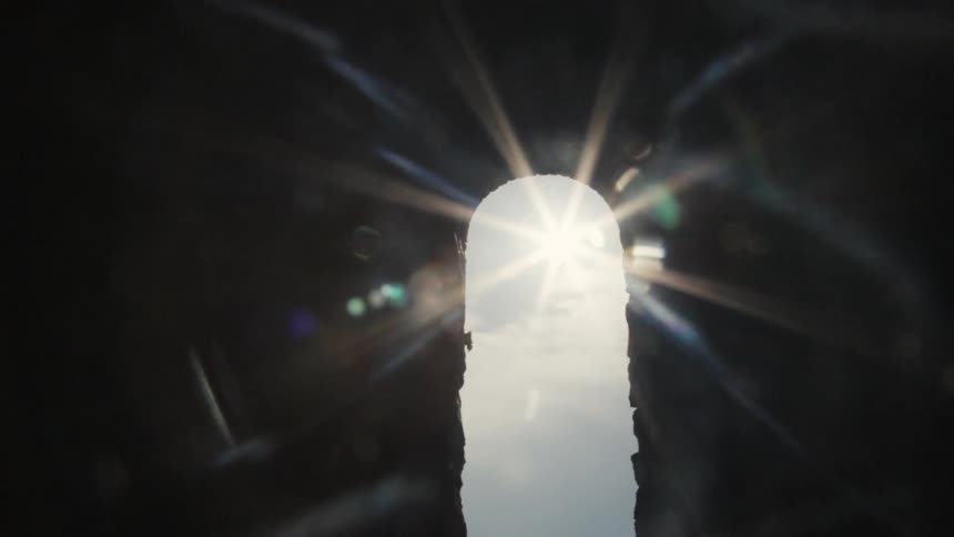 Bright sunlight streams and refracts through a narrow vertical opening in a dark structure to create a highcontrast silhouette and visual light effects
