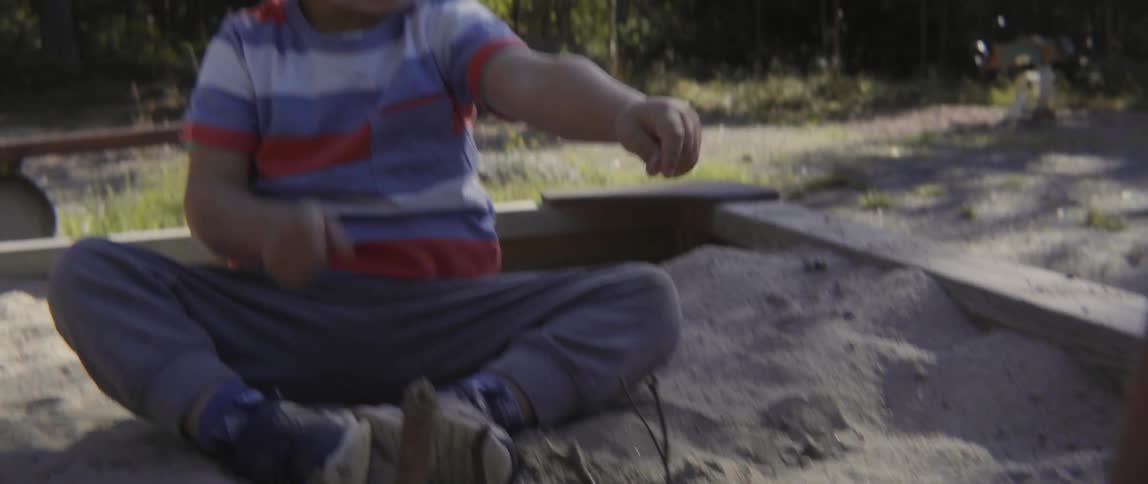 Happy toddler boy focusing on his play while sitting in a wooden sand pit.