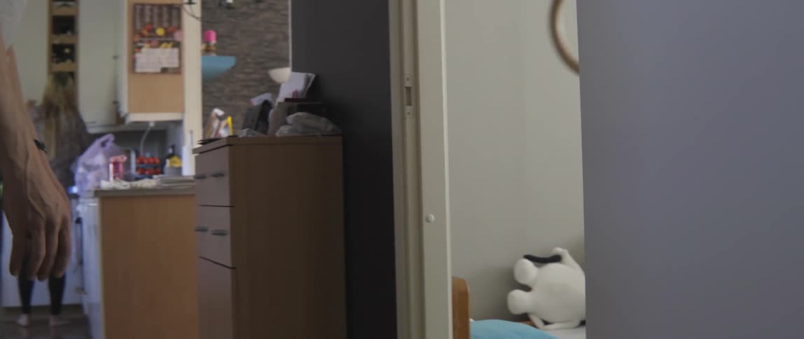 A man helps a young toddler boy swing from gymnastic handles inside a doorway.