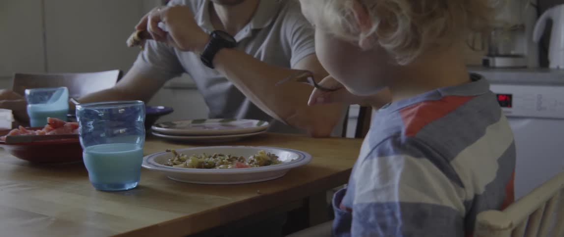 Young father and boy having a healthy snack at the dining table indoors.