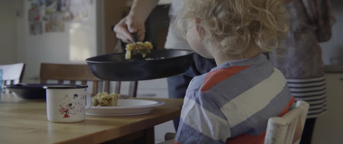 Young mother scooping food for her toddler during a family meal in kitchen.