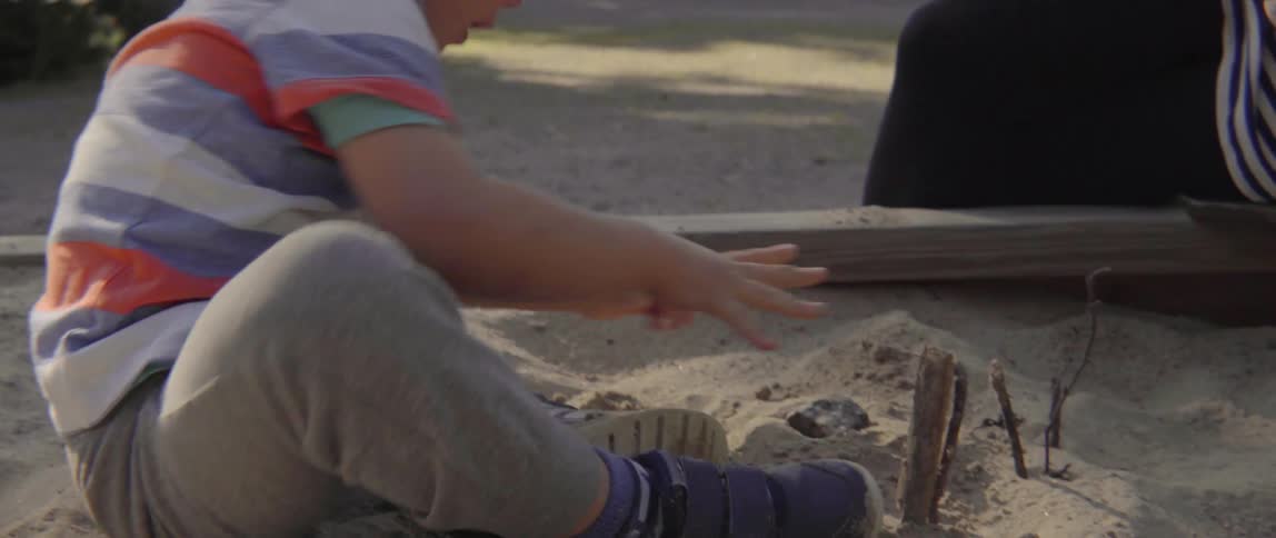 Young toddler boy focused on building and playing with natural elements in the sand.