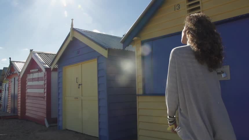 A young woman walking in front of a row of brightly colored beach sheds