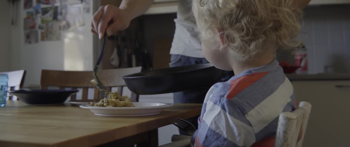 Young father scooping pasta into a bowl for his toddler in a bright kitchen.