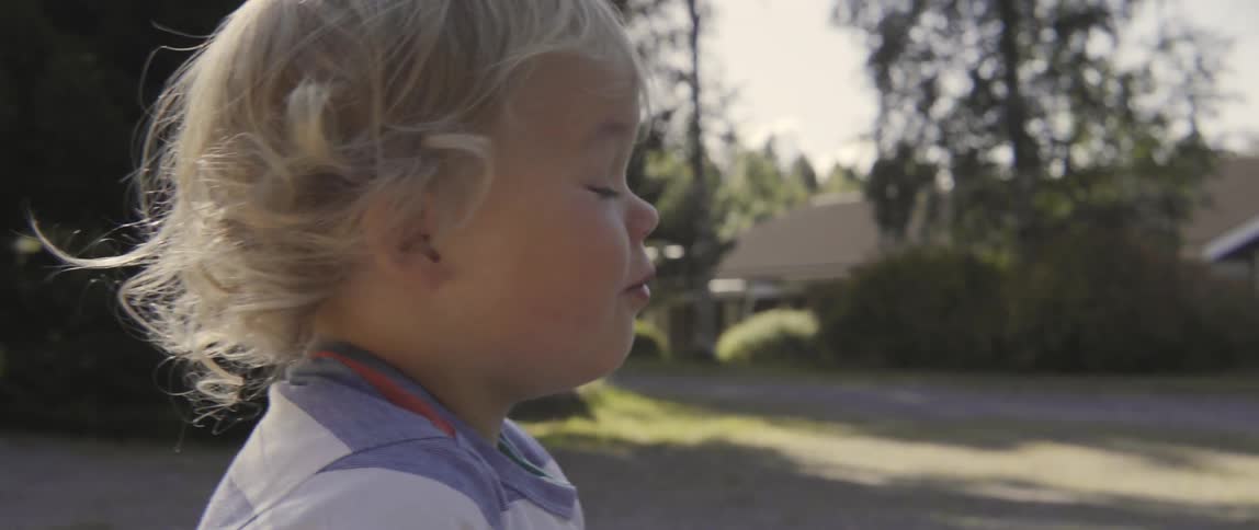 A young toddler boy pats the sand while sitting inside a large playground sandbox.