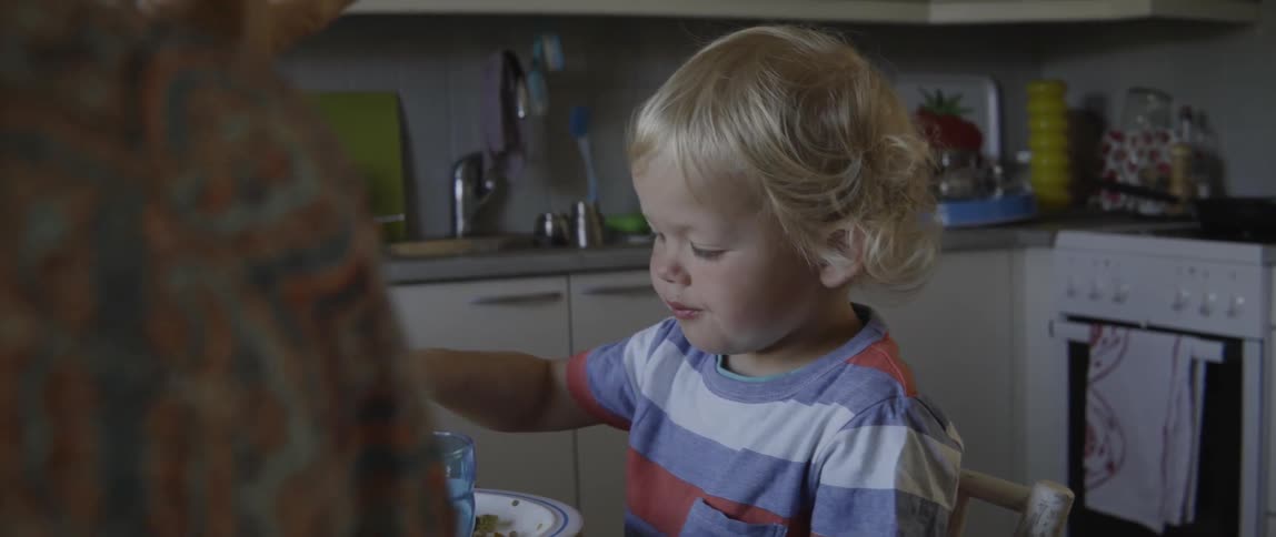 Happy toddler boy tasting his dinner while sitting in a chair at the table.