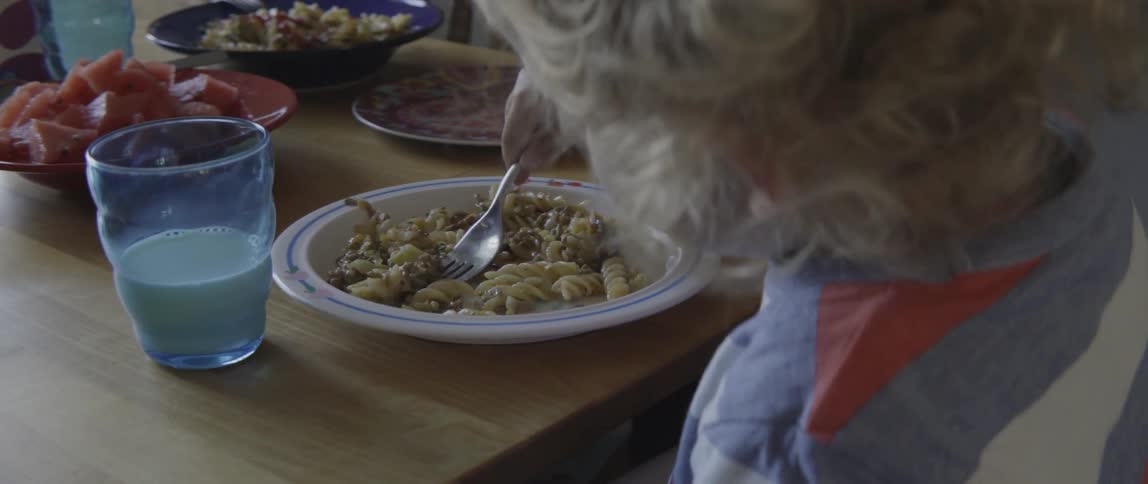 Happy toddler boy focusing on eating his dinner with a fork and milk.
