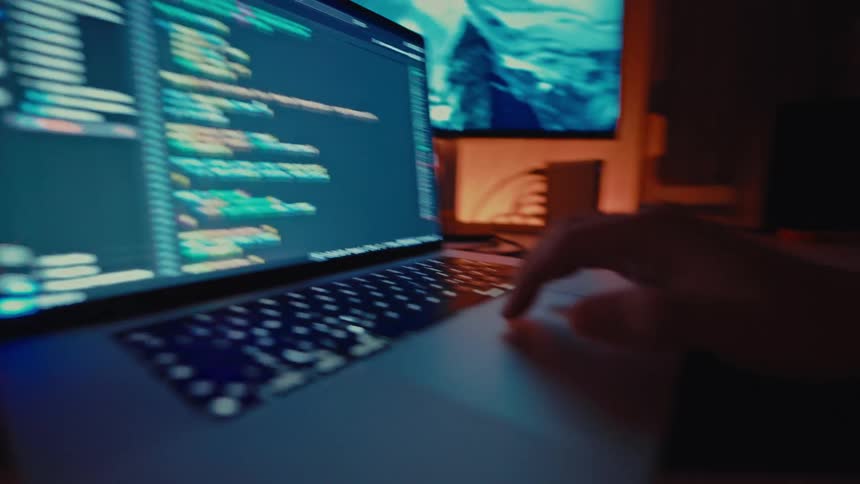 Close up of a person scrolling through a coding software while using a laptop computer in a room