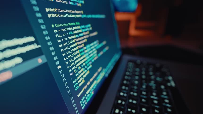 Closeup of laptop screen with programming code in dim light