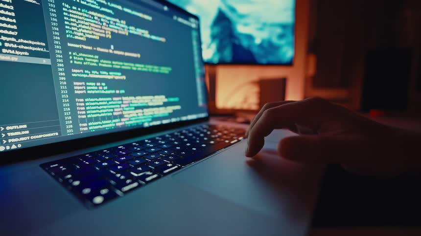 Close up of a person scrolling through a coding software interface while using a laptop computer in a room