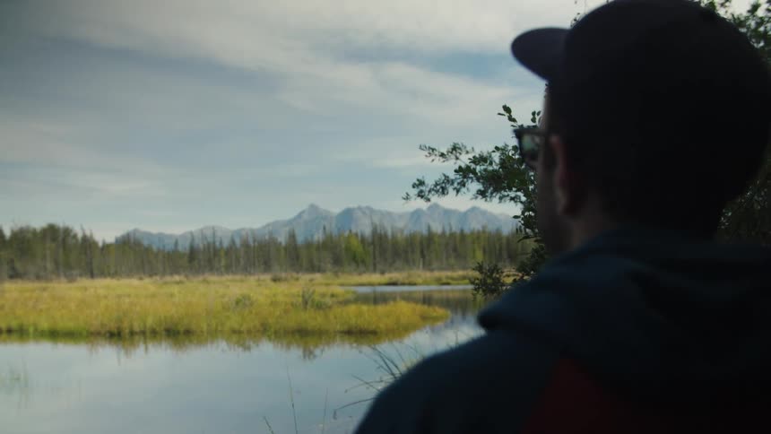 A man overlooks a calm lake surrounded by grasslands and distant mountains