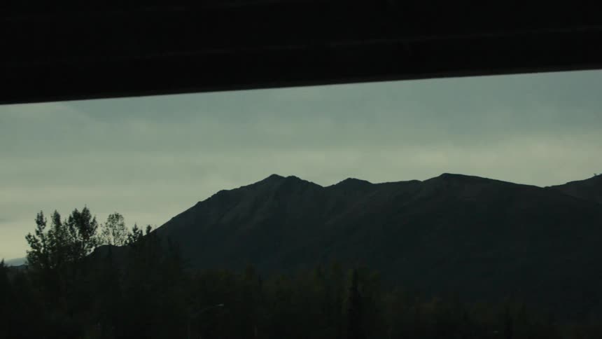 Wide shot of dark forested mountains under a cloudy overcast sky