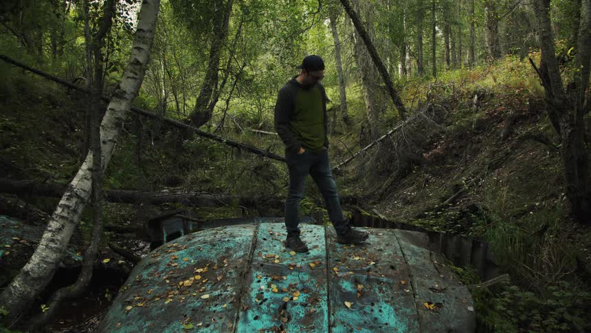 Man stands on a large piece of debris sitting in a stream in a forest on an autumn day