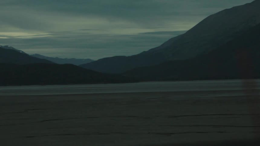 A mountain landscape lies beneath an overcast sky at dusk