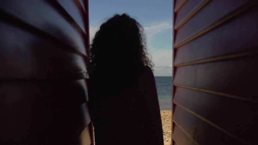 Woman walking between two buildings towards the beach