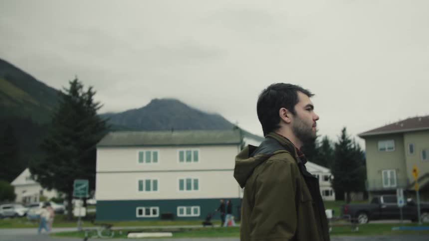 Man in a jacket looking toward the horizon in an urban area surrounded by trees and mountains